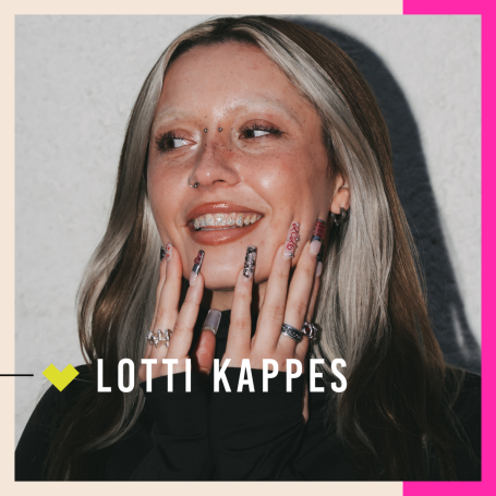 Lotti Kappes lächelt, trägt auffällige Nägel und posiert mit einer Hand an ihrem Gesicht.